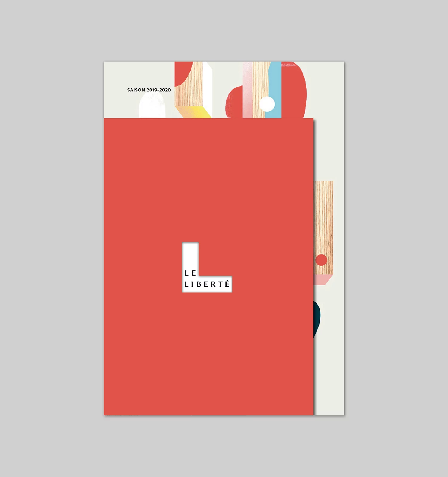 Brochure annuelle de la Scène Nationale, côté Le Liberté, avec la forme associée au logo Le Liberté en découpe au centre d'une couverture en aplat rouge