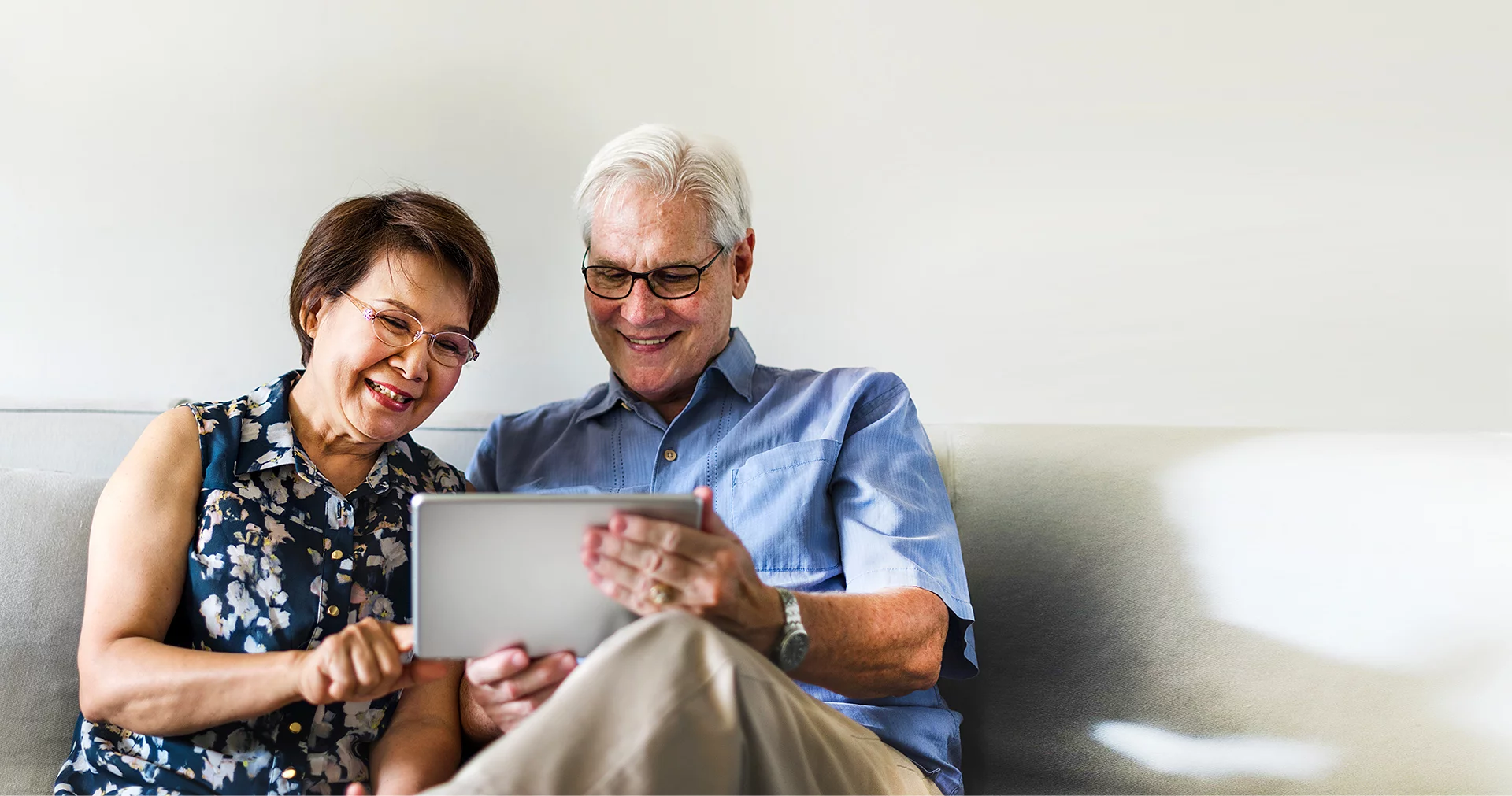 Couple de retraités souriants assis sur un canapé devant une tablette