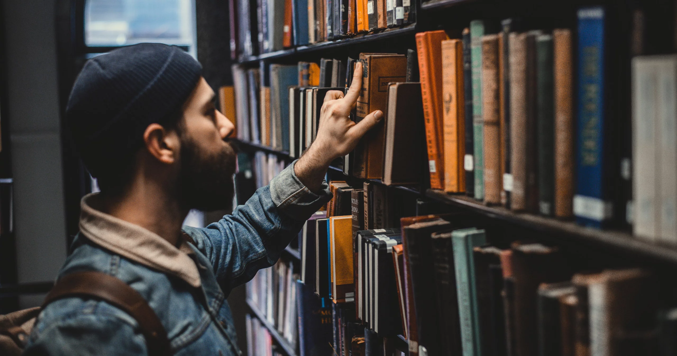 Photo d'un jeune homme attrapant un livre sur une étagère d'une bibliothèque