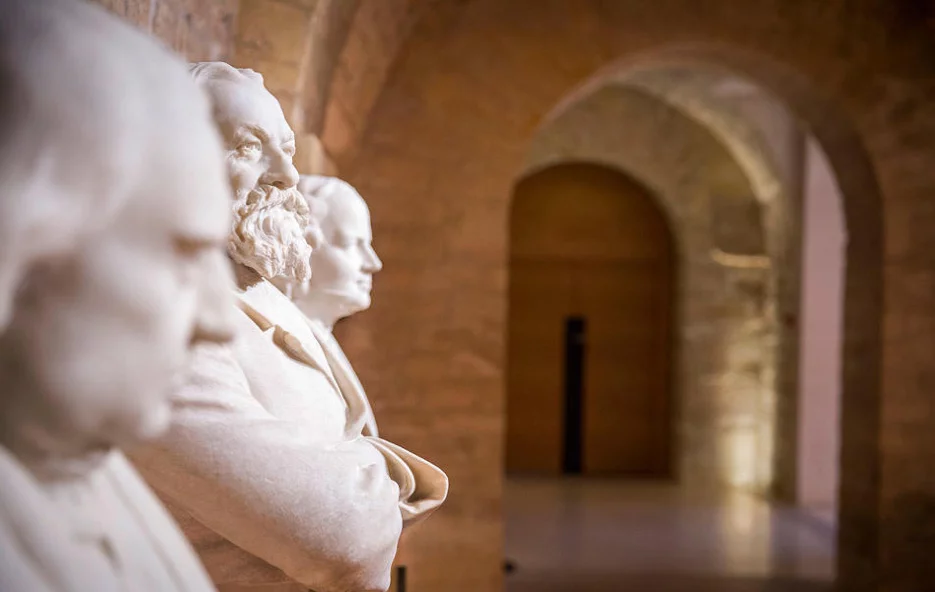 Une photo prise dans l'enceinte du collège de France. On y voit 3 statuts dans un couloir.