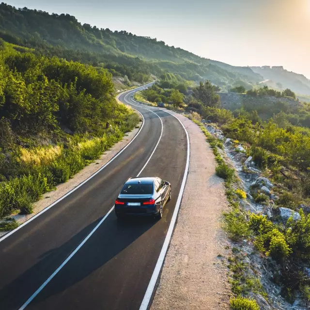 Vue d'une voiture qui roule sur une route dégagée et ensoleillée. Représente la puissance des batteries Steco, spécialiste de la batterie en France.